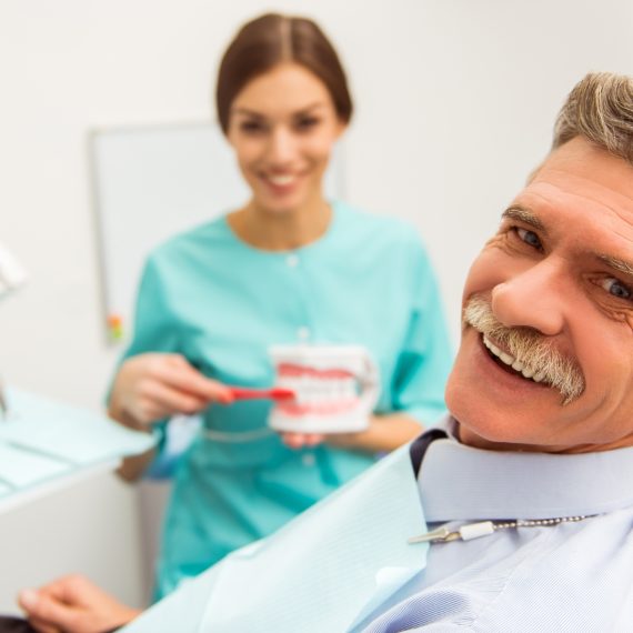 Smiling senior patient with a dental assistant holding dentures